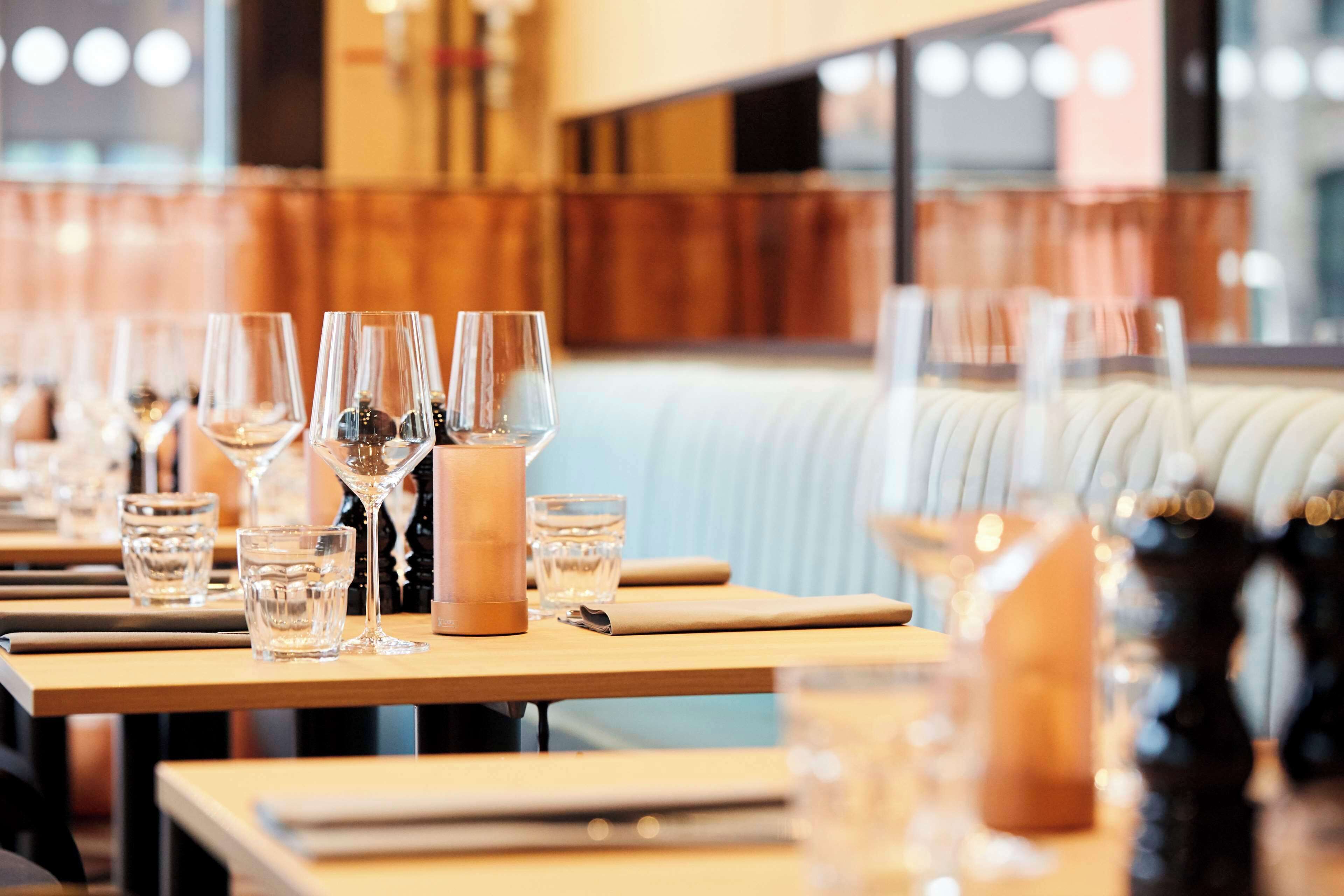 Een restaurantsetting met gedekte tafels, met helder glaswerk en servetten.