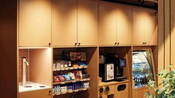Ein Selbstbedienungskiosk mit Kaffeeautomat und gekühlten Getränken, umgeben von Regalen voller Snacks und Erfrischungen.