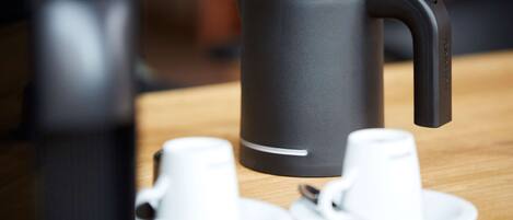 A coffee maker on a table with two white cups and saucers.