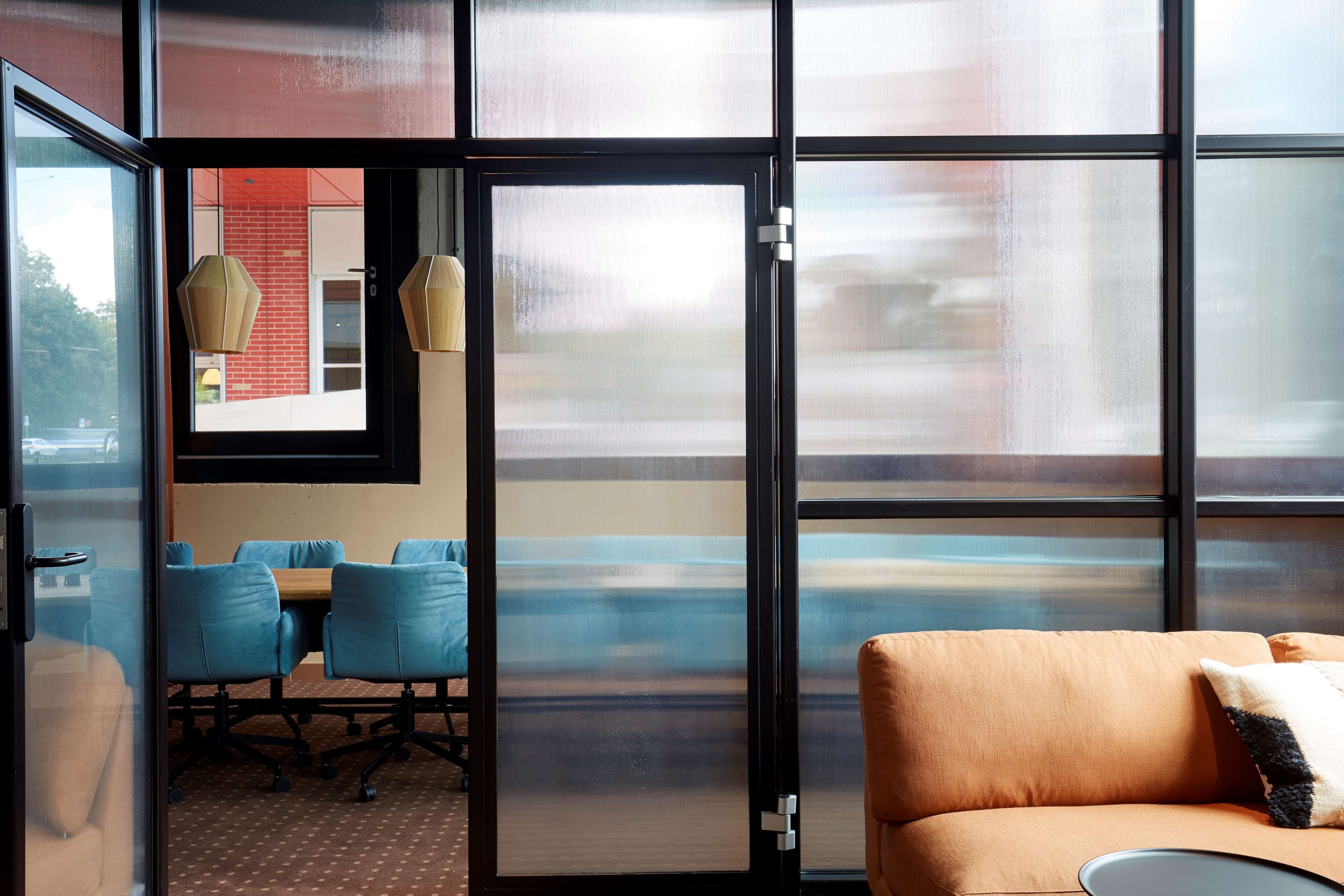 A modern room with a large glass door, a sofa, a table with chairs, and hanging lamps.