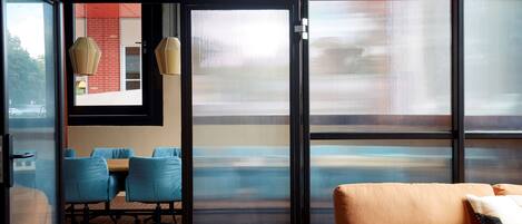 A modern room with a large glass door, a sofa, a table with chairs, and hanging lamps.