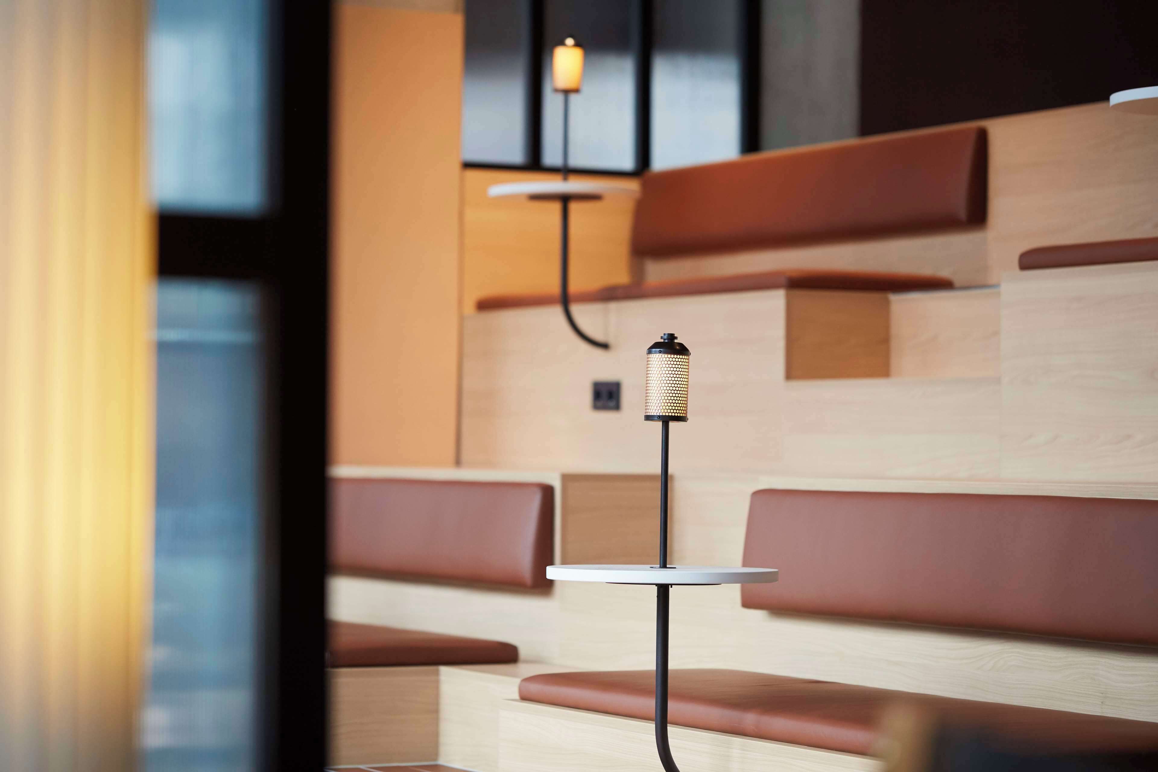 A modern interior with wooden panel walls, brown cushioned seating, and a small round table with a hanging light fixture.