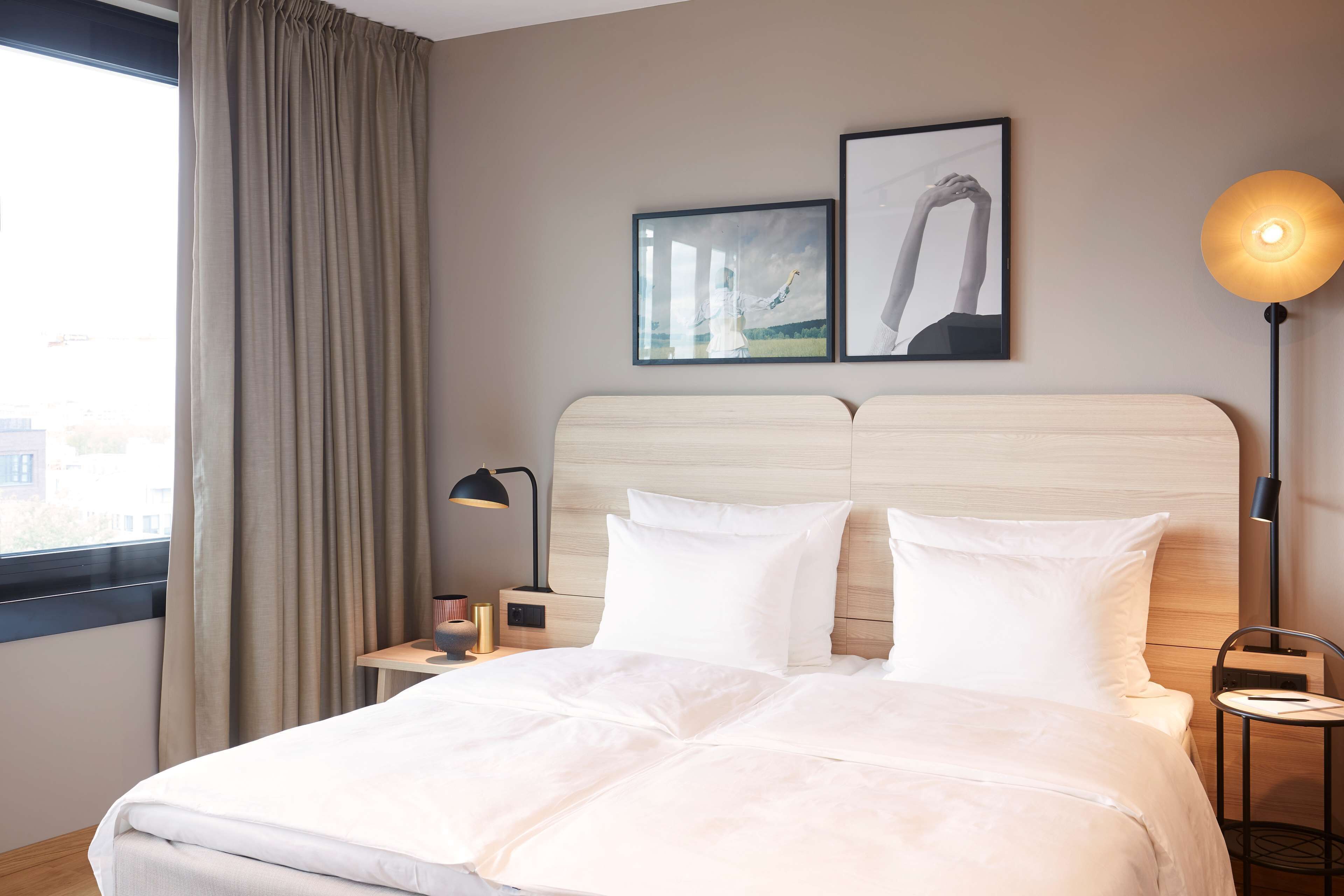 A hotel room with a large bed, a nightstand with a lamp, a chair, and two framed pictures on the wall.