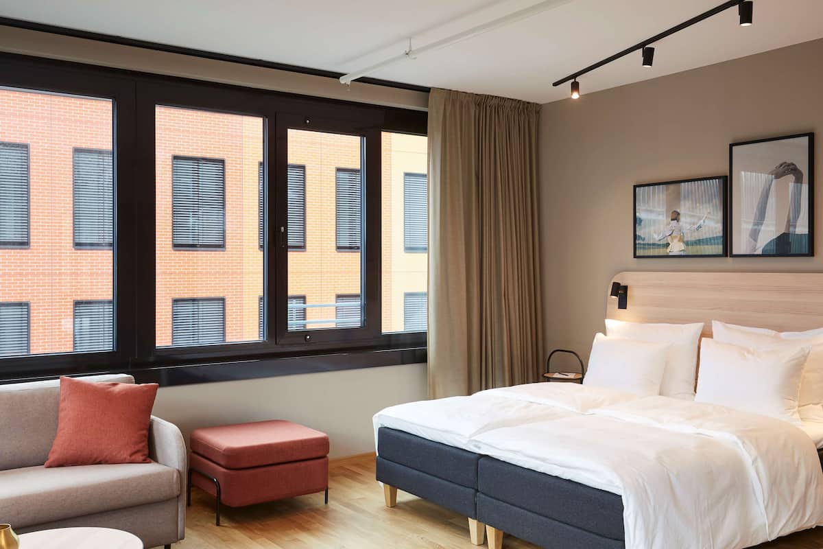 Moderni hotellihuone, jossa on suuri ikkuna, sänky, sohva ja pieni pöytä.