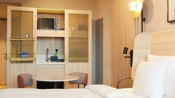 Ein kleines Hotelzimmer mit einem Bett, einem Esstisch und einer Mikrowelle.