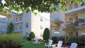 A courtyard with white Adirondack chairs, a well-maintained lawn, and a building with multiple balconies. - Enjoy the Scenery & Attractions of Branson! Sept 4th - 11th (Branson)