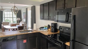 Uma cozinha moderna com armários escuros, bancada de granito, micro-ondas embutido, geladeira e cafeteira.