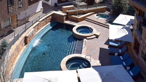 Een dakzwembad met meerdere jacuzzi's en ligbedden, omgeven door stenen muren en een helderblauw zwembad.
