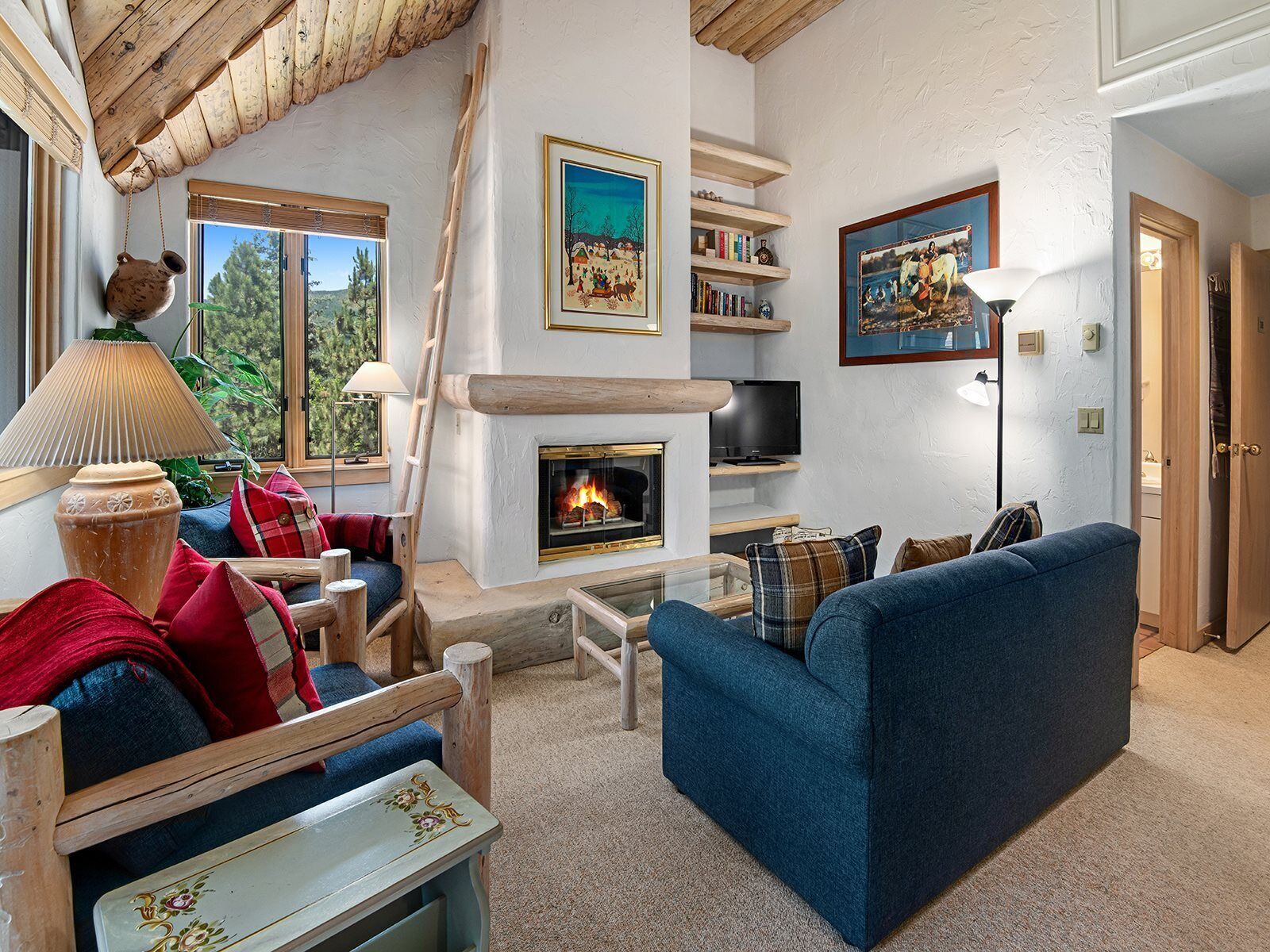 A cozy living room with a fireplace, blue sofa, wooden furniture, and a bookshelf.