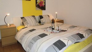 A neatly made bed with a striped blanket, a bedside table with a lamp, and a bottle of wine on the nightstand. - Alcazar by Interhome (Saas-Grund)