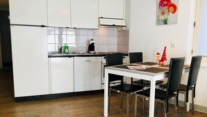 A modern kitchen with white cabinets, a dining table with four chairs, and a small Christmas tree decoration. - Alcazar by Interhome (Saas-Grund)