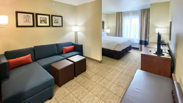 A hotel room with a sofa, two small tables, a bed, a desk with a computer, and a TV. - Comfort Inn & Suites Harrah (Harrah)