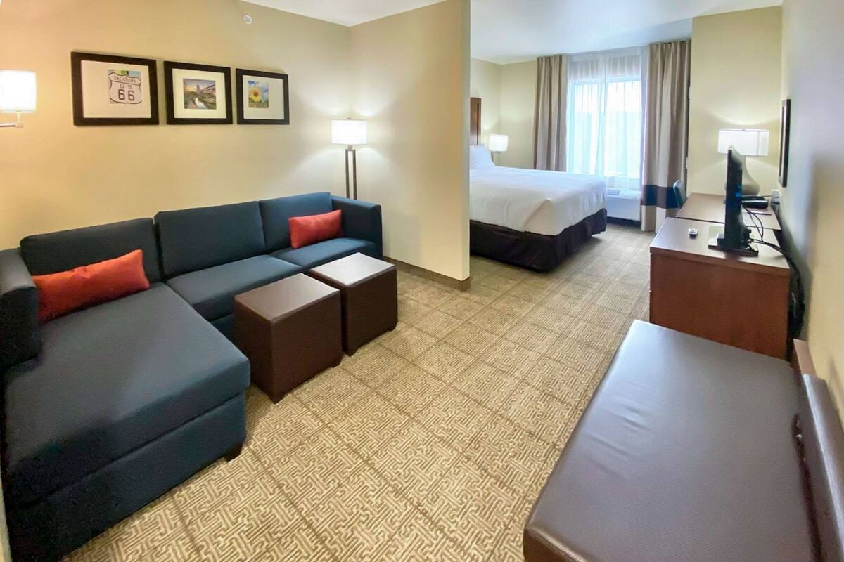 A hotel room with a sofa, two small tables, a bed, a desk with a computer, and a TV.
