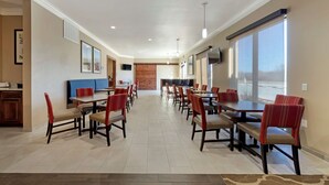 A spacious dining area with multiple tables and chairs, a wooden accent wall, and large windows providing natural light. - Comfort Inn & Suites Harrah (Harrah)