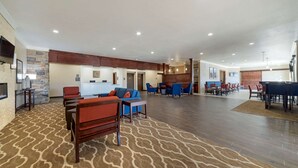 A spacious lobby with a patterned carpet, multiple seating areas with sofas and chairs, a kitchen area in the background, and a fireplace on the left. - Comfort Inn & Suites Harrah (Harrah)