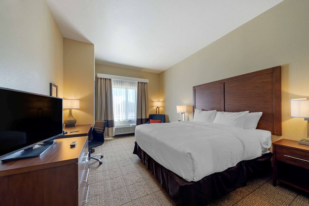 A hotel room with a large bed, a TV on a desk, a chair, and a window with curtains.