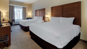 A hotel room with two beds, a desk, a chair, a lamp, and a window with curtains.