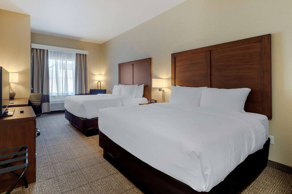 A hotel room with two beds, a desk, a chair, a lamp, and a window with curtains.