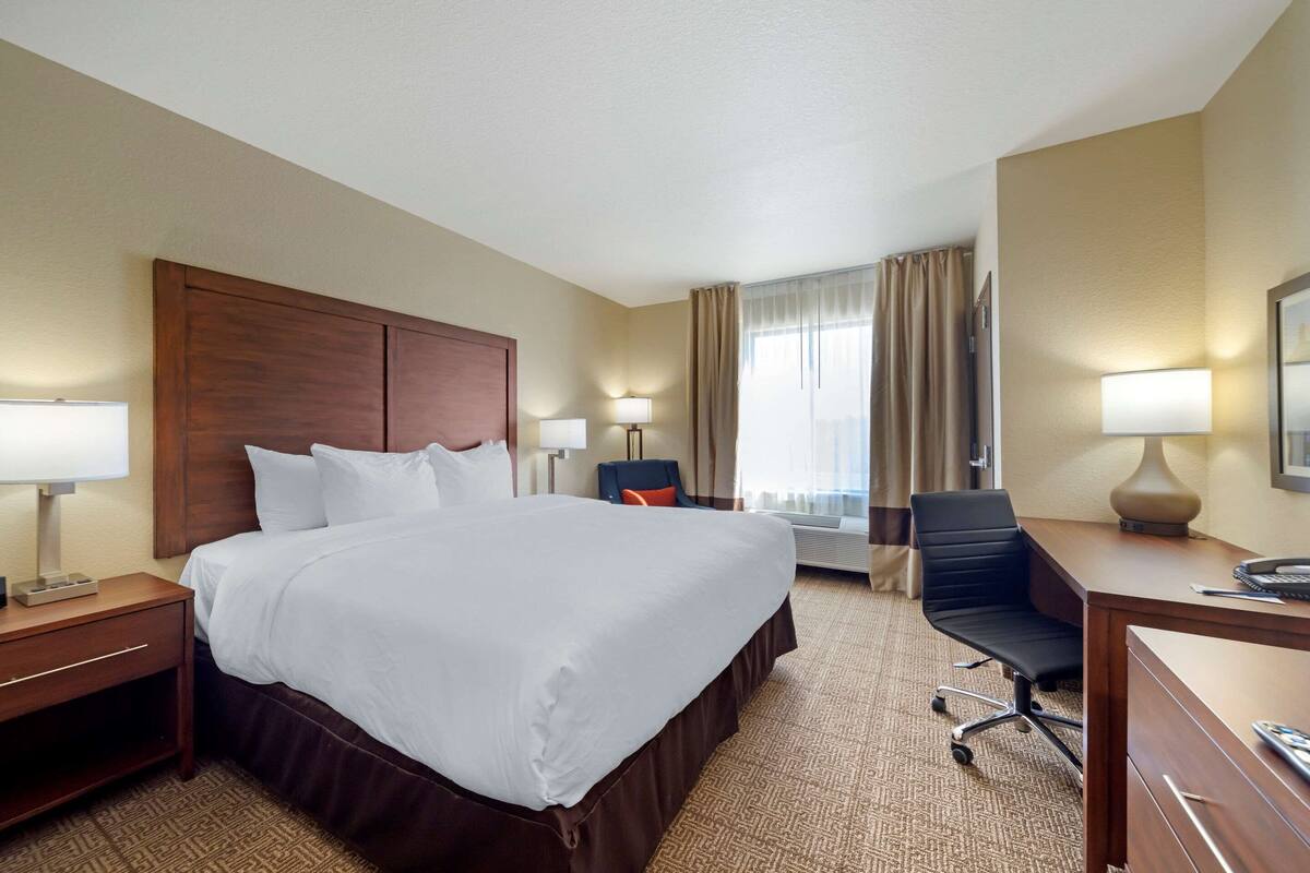 A hotel room with a large bed, a desk, a chair, and two lamps.