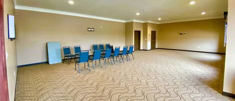 A large, empty conference room with a patterned carpet, blue chairs, and beige walls.