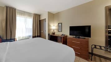 Ein Hotelzimmer mit einem großen Bett, einem Schreibtisch mit Lampe, einem Fernseher und einem Kleiderschrank.
