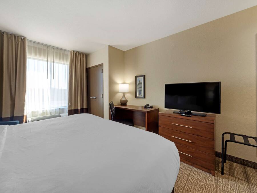 Ein Hotelzimmer mit einem großen Bett, einem Schreibtisch mit Lampe, einem Fernseher und einem Kleiderschrank.