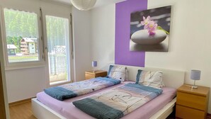 Une chambre à coucher avec un lit, deux tables de chevet, une fenêtre et un tableau accroché au mur.