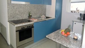 Une cuisine de taille réduite avec des meubles bleus, un plan de travail en granit, un four en acier inoxydable et une petite fenêtre donnant sur l’extérieur.
