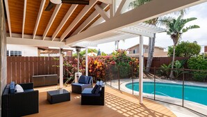 Ein überdachter Außenbereich mit Holzboden, schwarzer Rattanmöbel und einem Pool.