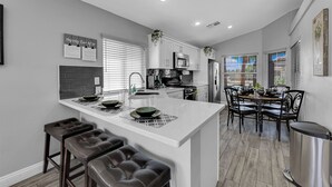 A modern kitchen with a large island, bar stools, and a dining area with a table and chairs.