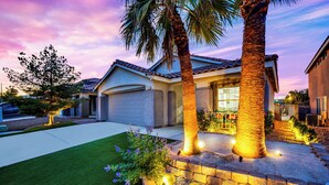 A residential house with a garage, a well-maintained lawn, and a landscaped garden with palm trees and flowers.