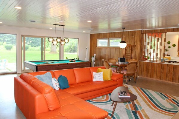A modern living room with a pool table, orange sectional sofa, and a pool.