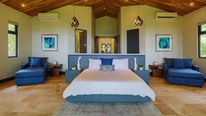 Un dormitorio con una cama grande, dos sofás azules, techo de madera y obras de arte en las paredes.