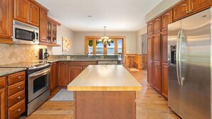 Une cuisine dotée de meubles en bois, d’appareils électroménagers en acier inoxydable, d’un grand îlot central et offrant une vue par la fenêtre.