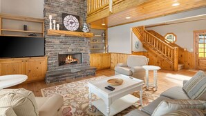 Un salon chaleureux avec une cheminée en pierre, des poutres apparentes, un téléviseur et un escalier.