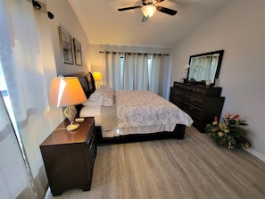 Une chambre à coucher comprenant un lit, des lampes de chevet, une commode, un ventilateur de plafond et un miroir.
