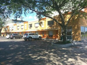 A multi-story building with a yellow facade, parked cars, and a tree in the foreground. - Chicago Lake Shore Hotel (Chicago)
