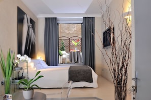 Une chambre d’hôtel moderne avec un grand lit, une petite table ornée d’un vase de fleurs et une vue sur un espace extérieur aménagé avec une table et des chaises.