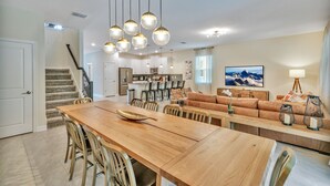 A spacious kitchen with a central island, modern pendant lighting, and a dining area with a wooden table and chairs. - 7BD/5BA BRAND NEW Home w/pool close to Disney (Kissimmee)