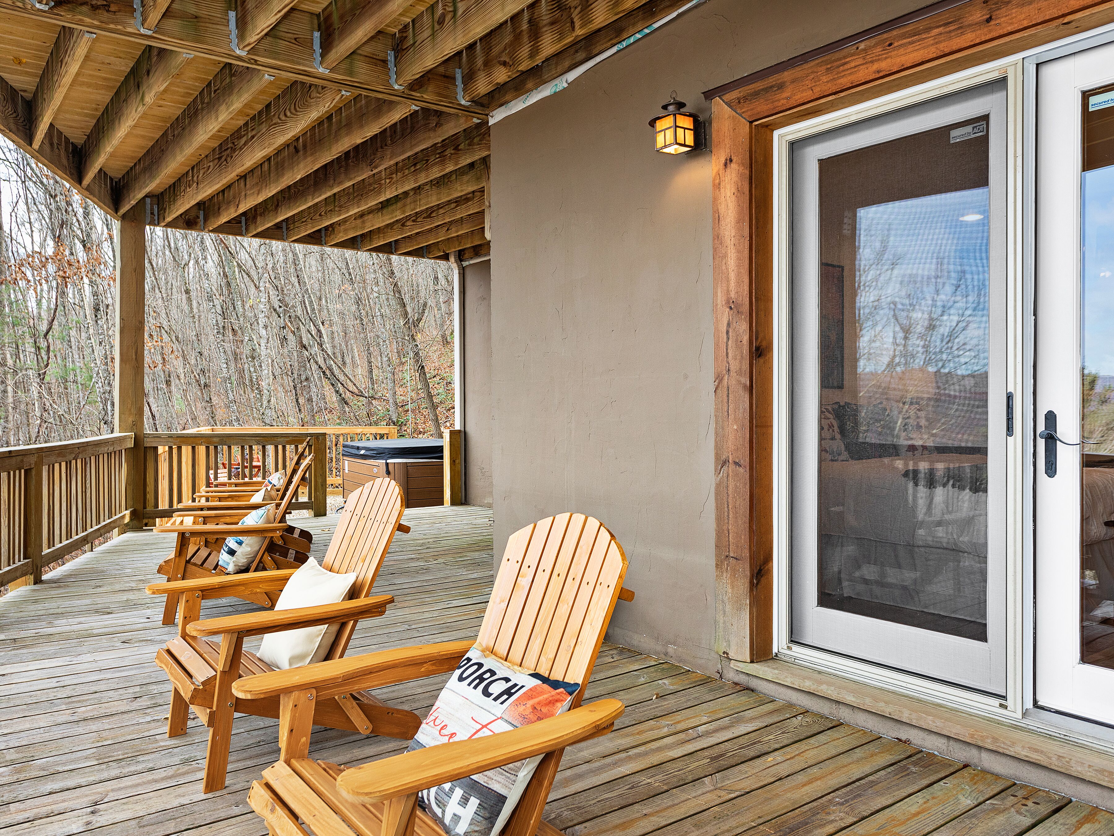 A wooden deck with Adirondack chairs and a table, a sliding glass door, and a wooden ceiling.
