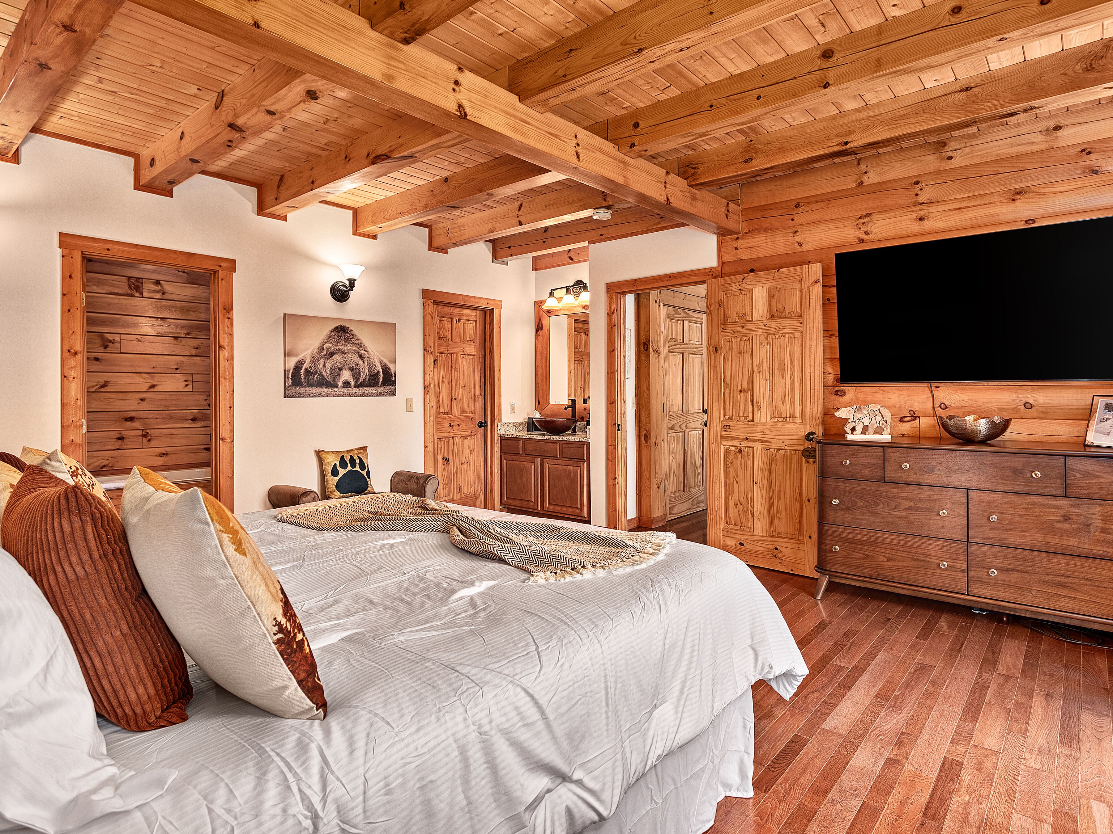 A bedroom with a wooden ceiling, a bed with patterned bedding, a dresser, and a large mirror.