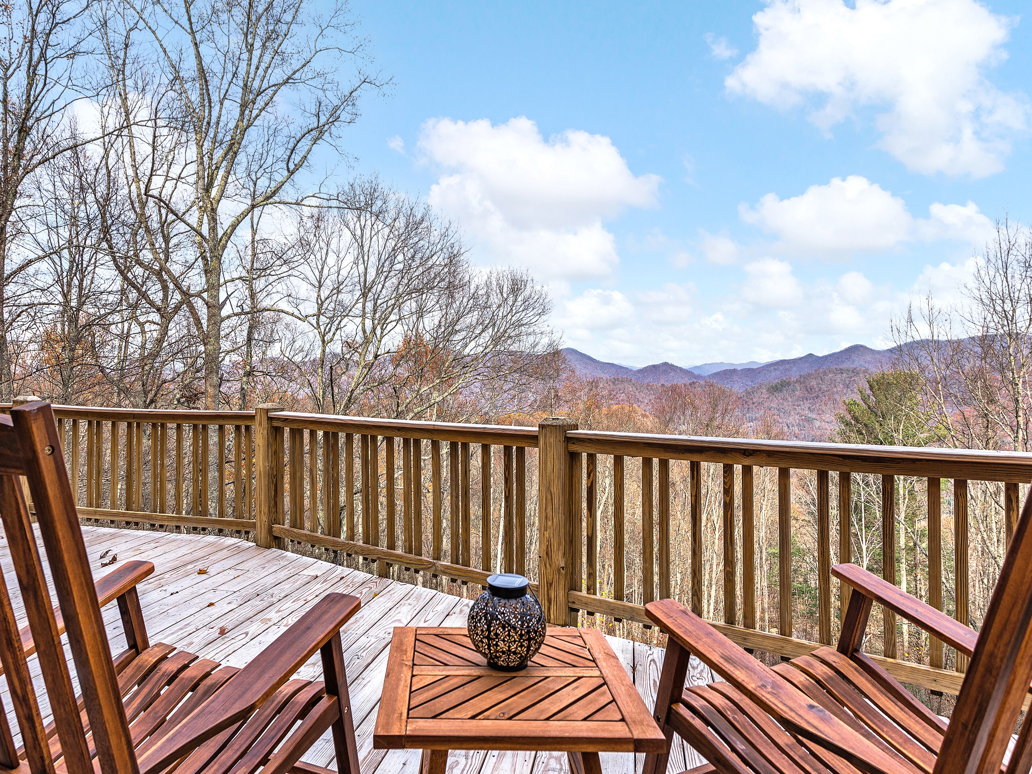 Una terraza de madera con mesa y sillas, con vista a un paisaje montañoso.