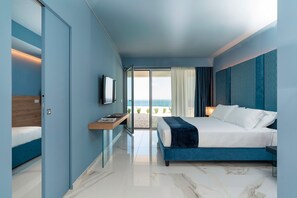 A modern hotel room with a bed, a desk, a TV, and a view of the beach.