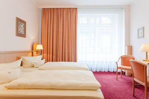 A hotel room with two beds, a large window with curtains, a desk with a chair, and wall-mounted lamps. - Hotel Benn (Berlin)