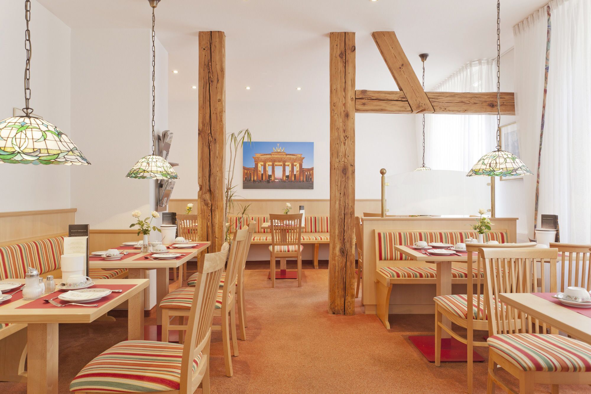A restaurant with wooden beams, striped upholstered benches, and hanging lamps.