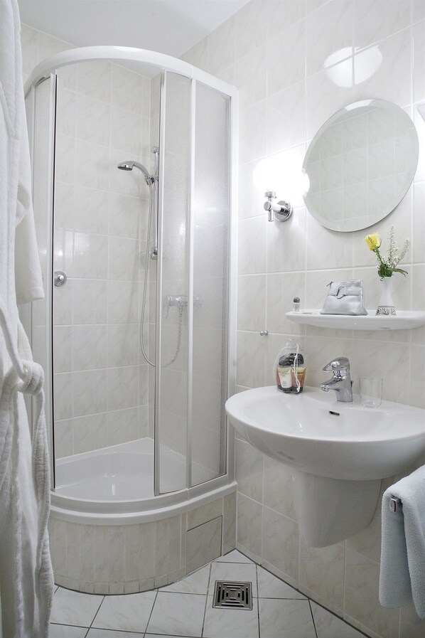 A modern bathroom with a glass-enclosed shower, a white sink, and a round mirror. - Hotel Benn (Berlin)