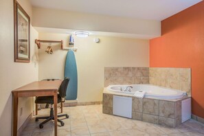 A bathroom with a wooden desk, a chair, a blue towel, a bathtub, and a framed picture on the wall. - Rodeway Inn and Suites Macon (Macon)