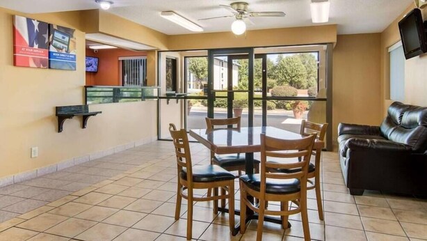 Un comedor con mesa y sillas de vidrio, ventilador de techo y sofá de cuero negro.