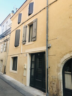 Un immeuble à la façade beige, avec des volets noirs aux fenêtres et une porte noire portant le numéro 16.
