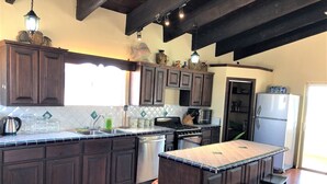 Una cocina con armarios de madera oscura, salpicadero de azulejos, una isla central con taburetes, una estufa, un fregadero y un refrigerador.